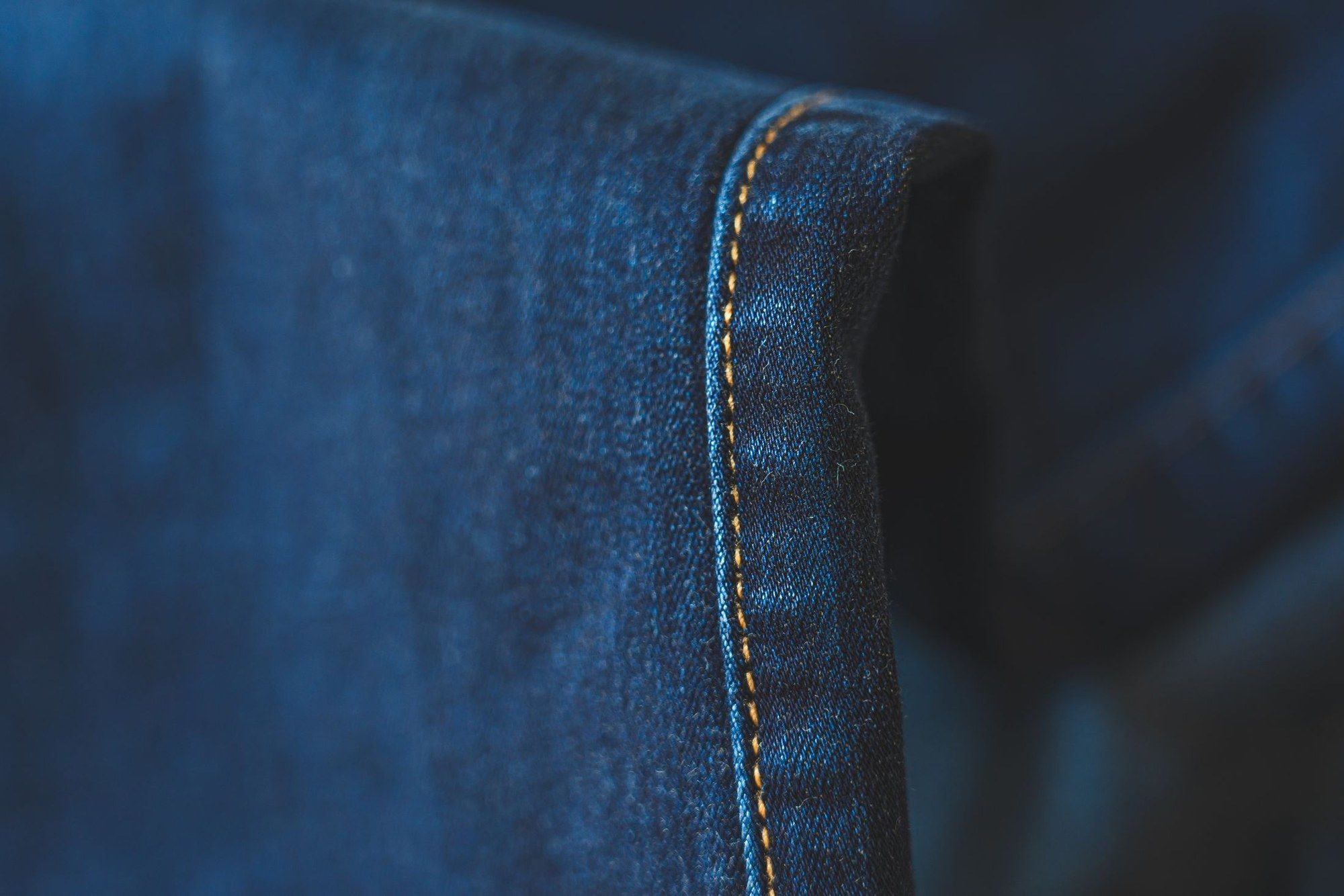 Saum einer dunkelblauen Jeans mit gelber Naht, aus der Nähe