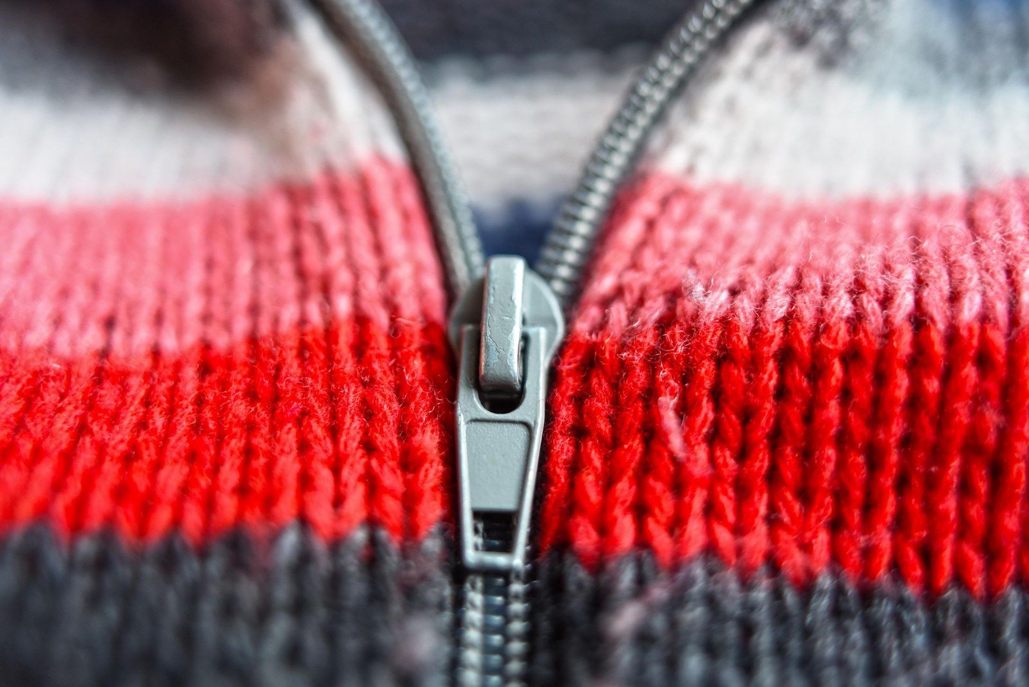 Grauer Reißverschluss in einer rot-weiß-grau gestreiften Strickjacke, aus der Nähe